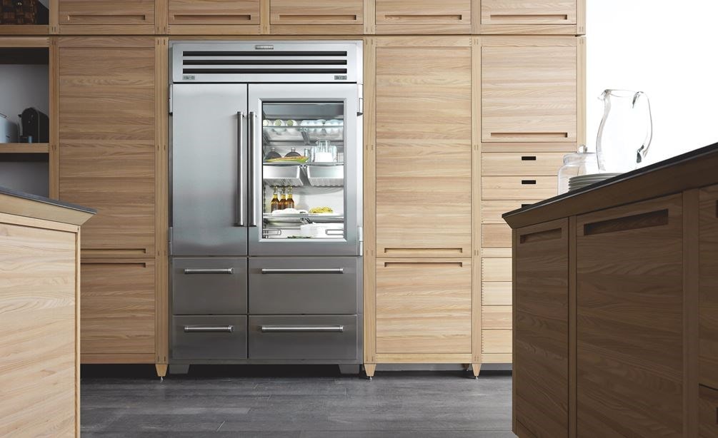 stainless steel sub-zero pro series french door fridge with glass panel door and solid door with bottom freezer drawers surrounded by kitchen cabinets